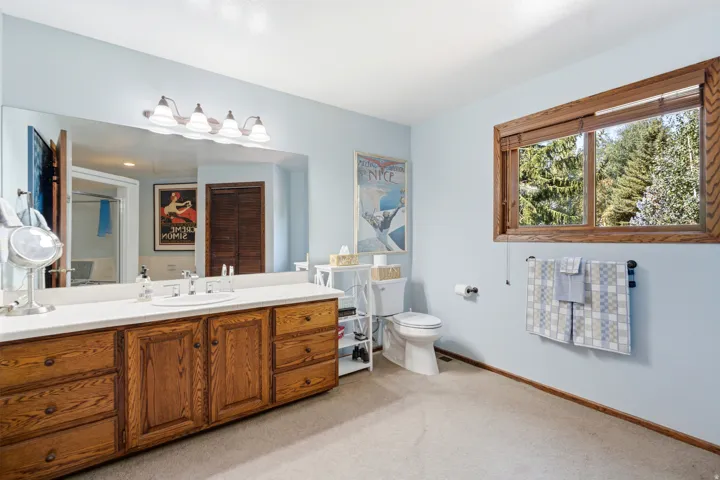 Spa-inspired primary bathroom featuring a double vanity with wood cabinetry, dual vessel sinks, extensive counter space, and large framed mirror with integrated lighting