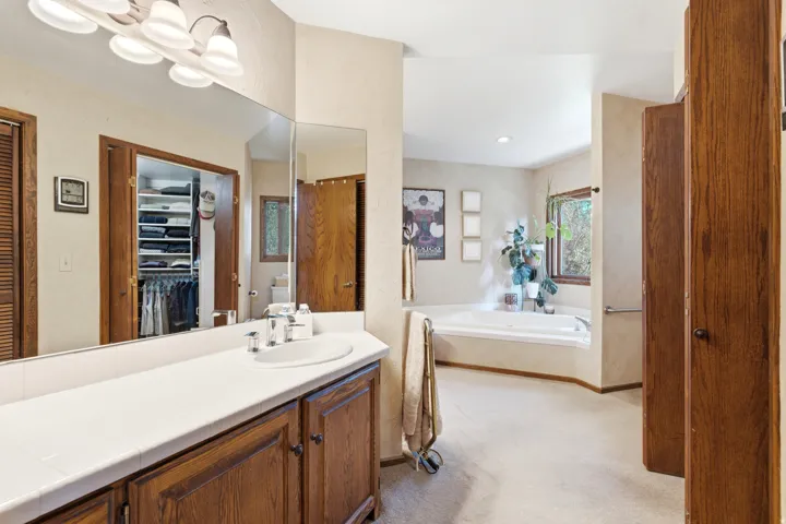 Primary with double vanity with a white countertop and integrated sink, wood-finish cabinetry, and a large wall-mounted mirror