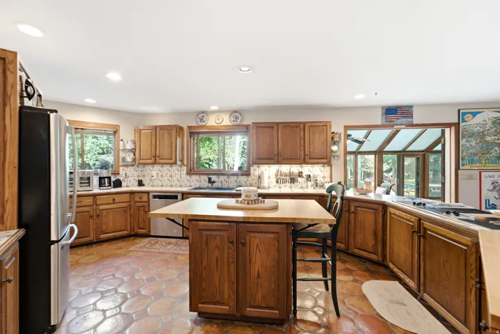 Kitchen featuring wood cabinetry, stainless steel appliances, a center island with seating, and terracotta tile flooring