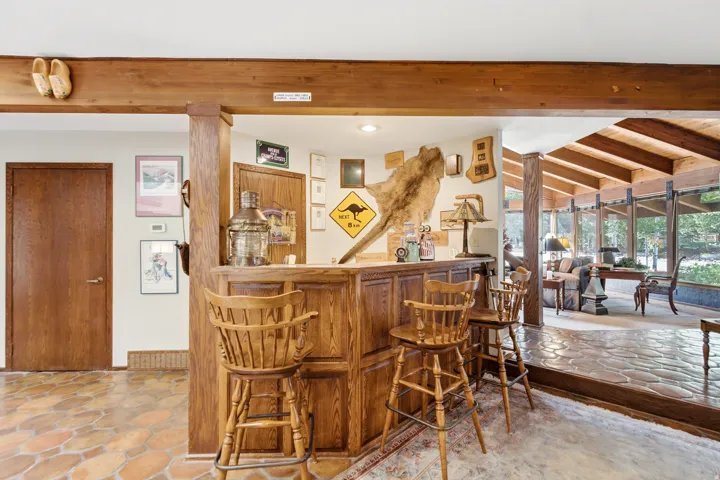 Wood-paneled built-in bar, exposed wood beams, and a sunroom with vaulted wood-paneled ceilings