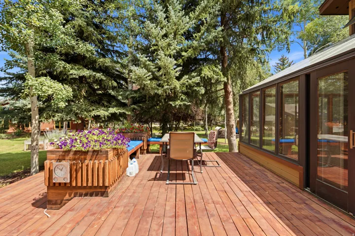 Expansive wood deck with built-in planters and bench seating, offering direct access to a sunroom with multiple window panels and exterior double doors