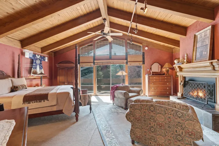 Primary with vaulted wood-paneled ceiling with exposed beams, full-height glass windows, and a built-in fireplace with a decorative mantel