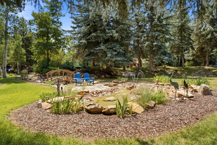 Landscaped backyard featuring a pond, a decorative fountain, and a wooden footbridge