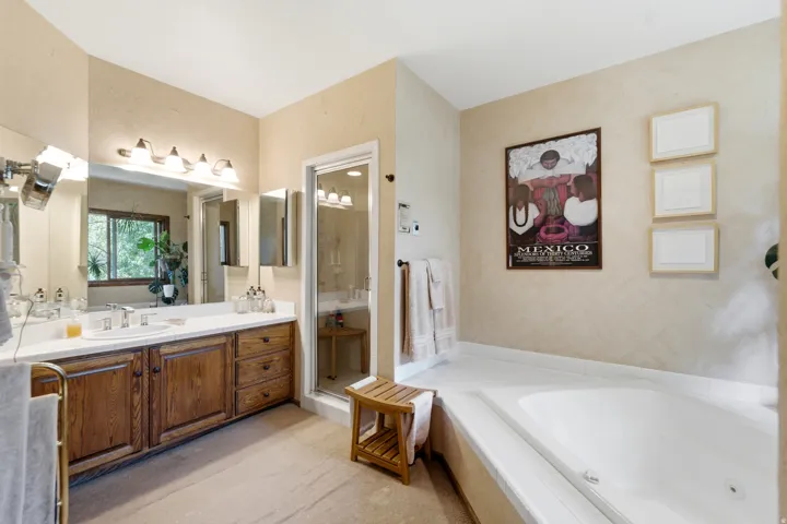 Primary with dual-sink vanity with wood-finish cabinetry, built-in soaking tub, glass-enclosed shower, and large wall-mounted mirror