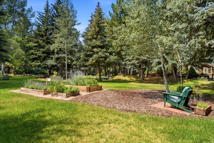 Expansive lawn area featuring multiple raised garden beds, mature trees, and a brick paver patio
