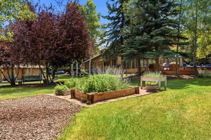 Expansive outdoor space featuring raised garden beds, a wood chip path, mature trees, and a multi-level deck