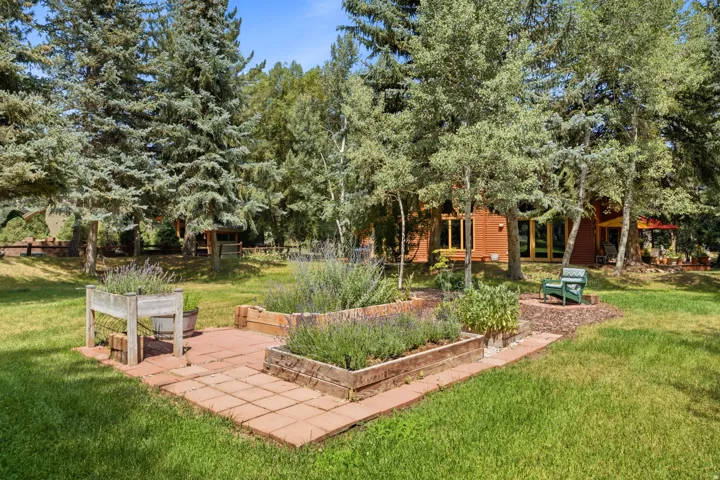 Expansive green lawn with mature trees and a dedicated garden area featuring raised planters