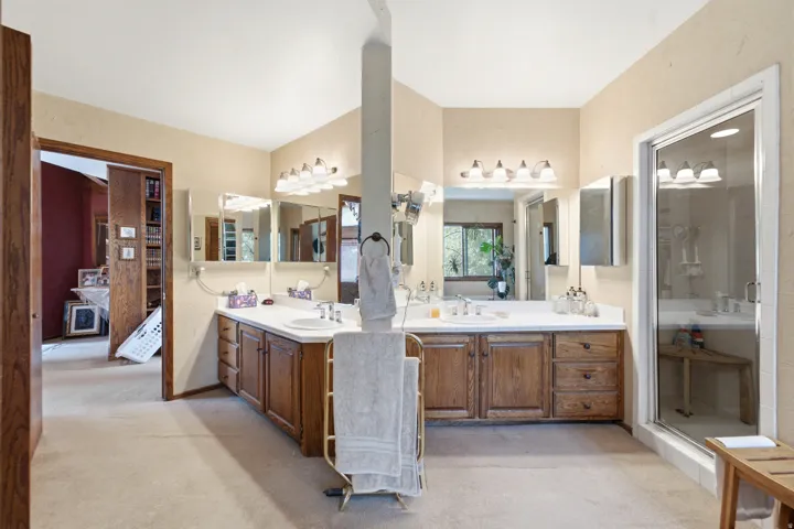 Primary with dual vanities with white countertops, wood-finish cabinetry, and framed mirrors