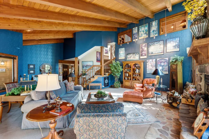 Vaulted ceilings with exposed wood beams, stone flooring, built-in fireplace, and a natural wood staircase