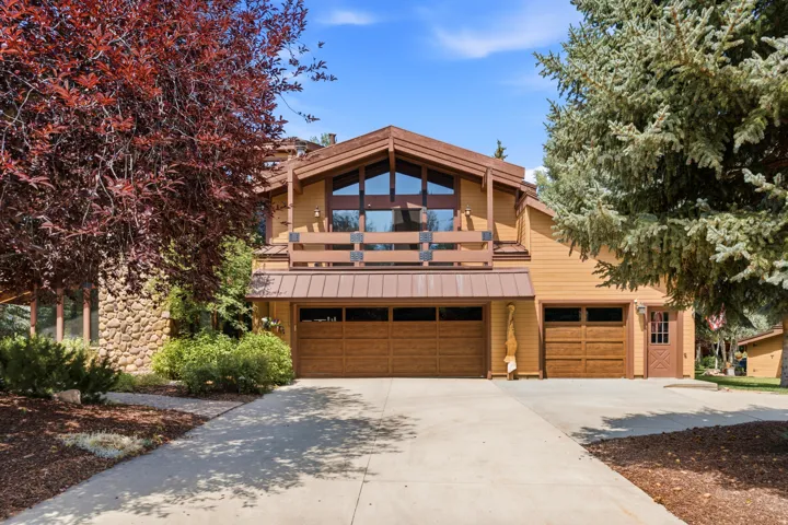 Exterior featuring a stone-clad facade, wood-finish siding, a multi-car garage with wood-finish doors, a balcony with a wood railing, and prominent gable windows