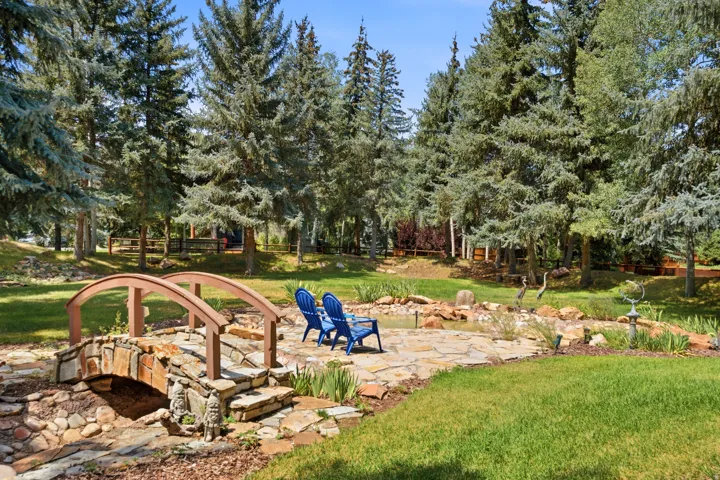 Manicured lawn with a stone-accented bridge, flagstone patio, and mature evergreen trees