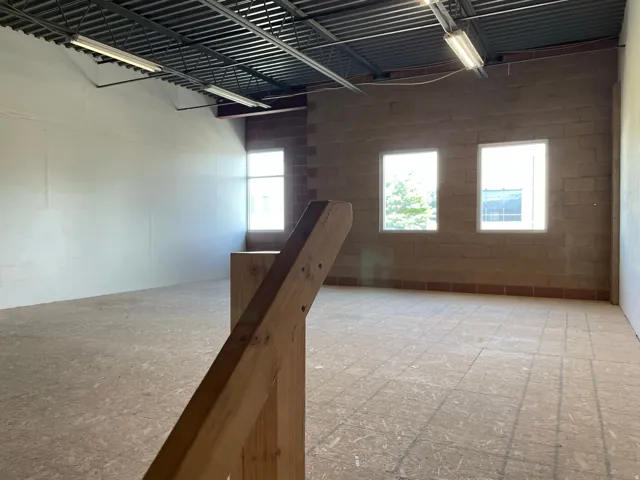 Spacious open floor plan with exposed industrial ceiling, polished concrete flooring, and abundant natural light from three large windows