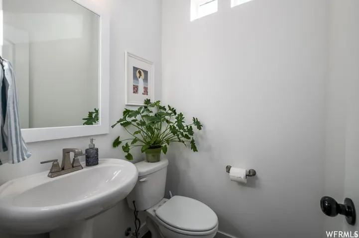 Pedestal sink with a two-handle faucet, wall-mounted mirror, and a toilet