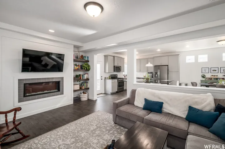 Living area featuring a rectangular electric fireplace with a gray tile surround, built-in shelving, wood-finish flooring, and recessed lighting
