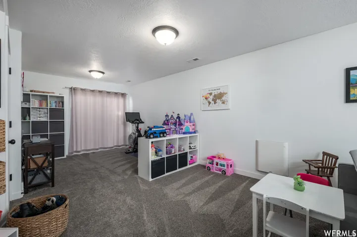 Recessed ceiling lighting, light gray wall-to-wall carpeting, white painted walls, and window with light-toned drapes