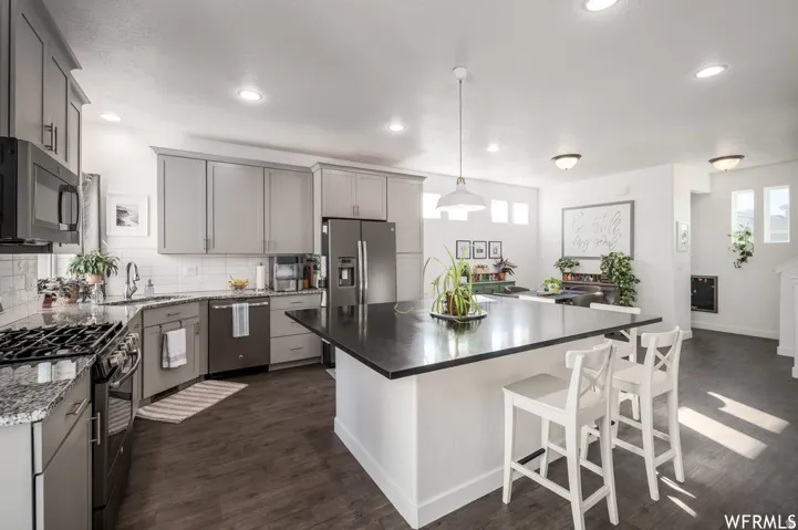 Contemporary kitchen featuring light gray cabinetry, dark granite countertops, stainless steel appliances, and wood-finish flooring