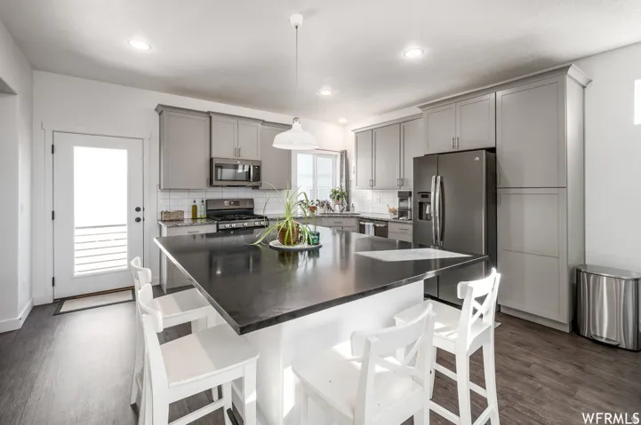 Kitchen featuring a large island with dark countertop, gray cabinetry, stainless steel appliances, and wood-finish flooring