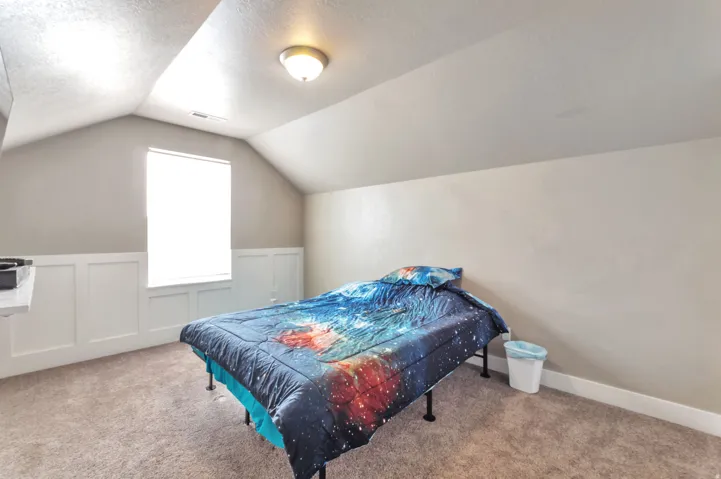 Sloped ceiling room featuring a window with blinds, wall paneling, and carpet flooring