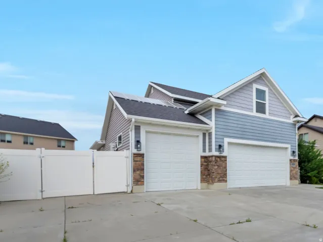 Fiber cement siding exterior with stone accents, two-car garage, concrete driveway, and white privacy fencing