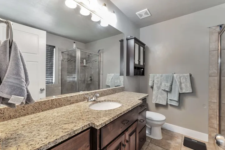 Vanity with a light-colored speckled countertop and undermount sink, dark wood-finish cabinetry, built-in medicine cabinet, and a tiled shower with a glass enclosure