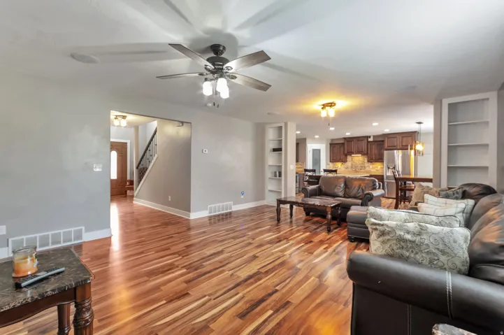 Spacious open-concept living area featuring hardwood flooring, ceiling fan with integrated lighting, and abundant natural light from multiple windows