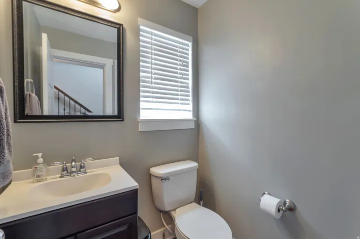 Modern bathroom featuring a sleek vanity with integrated sink and faucet, white porcelain toilet, framed mirror with integrated lighting, and a shuttered window providing natural light