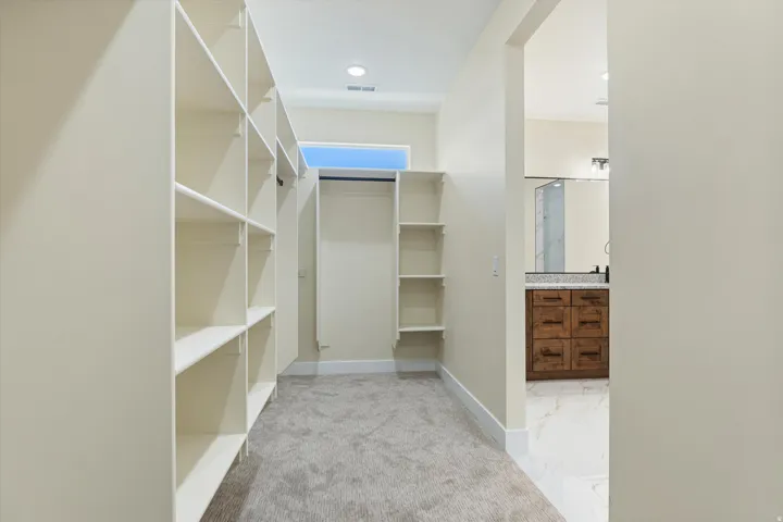 Spacious walk-in closet featuring extensive built-in shelving with white finish, carpeted flooring, and recessed ceiling lighting