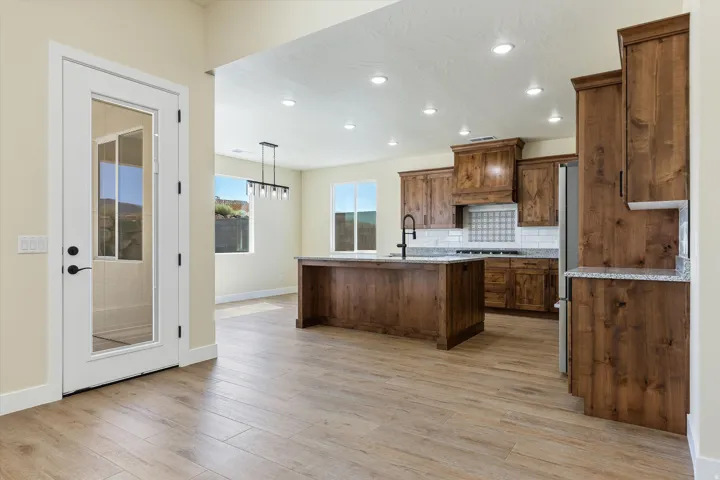 Spacious kitchen featuring rich wood cabinetry, a large center island with seating, stainless steel appliances, subway tile backsplash, and wood-finish flooring throughout