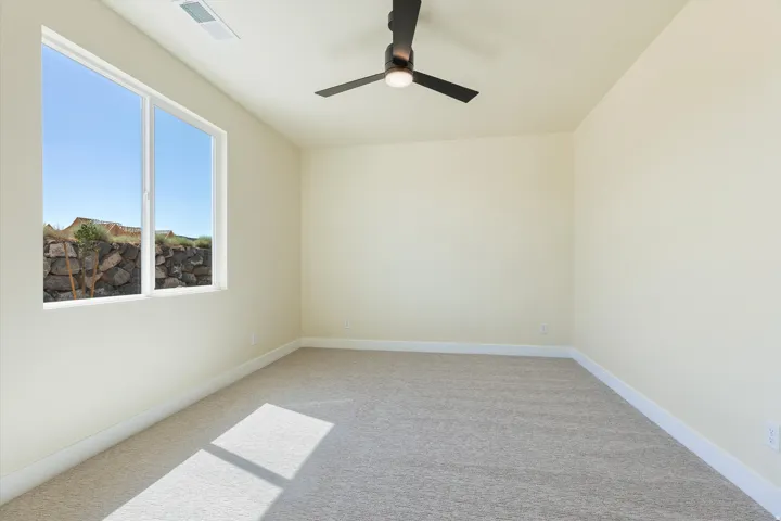 Bright corner bedroom with abundant natural light from dual windows, neutral wall finishes, ceiling fan, and neutral-toned carpeting with border detail