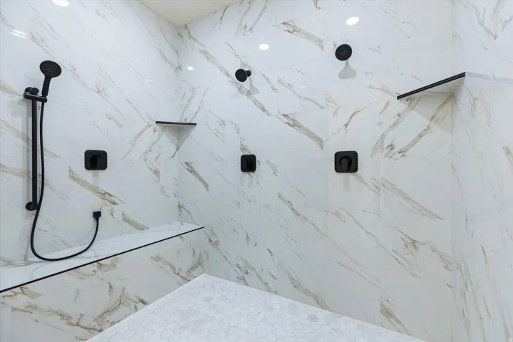 Spa-inspired shower enclosure featuring large-format marble-look tile walls, multiple body jets and rain showerhead with matte black fixtures, and recessed ceiling lighting for a luxurious bathing experience