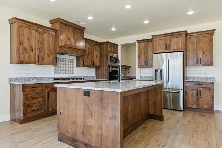 Chef's kitchen featuring custom wood cabinetry, stainless steel appliances, granite countertops, a large center island with seating, and recessed lighting throughout