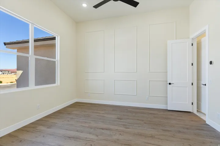 Bright, light-filled bedroom showcasing wood-finish flooring, large window with natural light, ceiling fan, and built-in closet storage with white panel doors