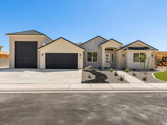 Modern single-story residence featuring a clean stucco exterior with peaked rooflines and dark-framed garage doors