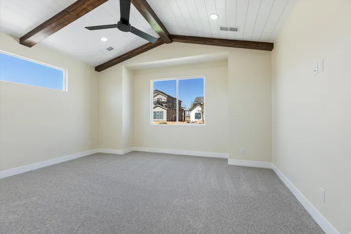 Spacious bedroom featuring soaring vaulted ceilings with exposed wood beams, a ceiling fan, and abundant natural light from dual windows