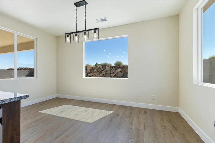 Bright, open dining area showcasing wood-finish flooring, abundant natural light from multiple windows framing scenic landscape views, modern pendant lighting fixture, and clean architectural lines throughout the space