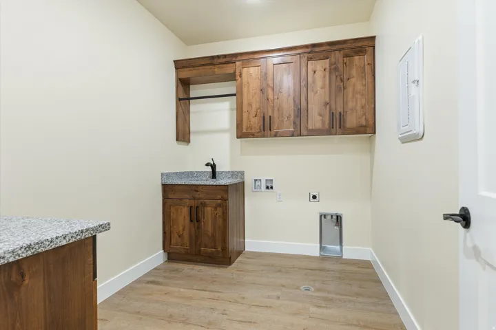 Utility room featuring custom wood cabinetry with matching upper storage, wood-finish flooring, granite-style countertop with integrated sink and faucet, and abundant natural lighting from recessed fixtures and wall outlets for convenient appliance placem