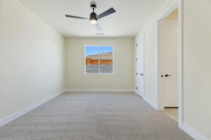 Spacious bedroom with neutral wall finishes, gray carpeting, ceiling fan with integrated lighting, and abundant natural light from a large window framing scenic outdoor views