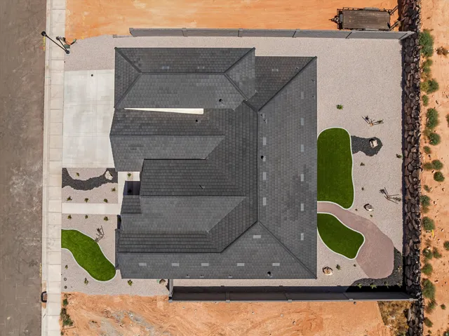 Aerial view showcasing a newly constructed residence with a distinctive multi-gabled roof featuring dark architectural shingles