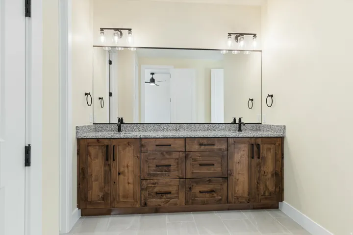 Primary Bathroom featuring a dual-sink vanity with wood cabinetry, gray stone countertop, and polished chrome hardware