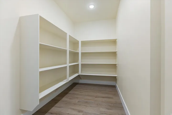 Expansive pantry with built-in shelving, wood-finish flooring, and recessed ceiling lighting