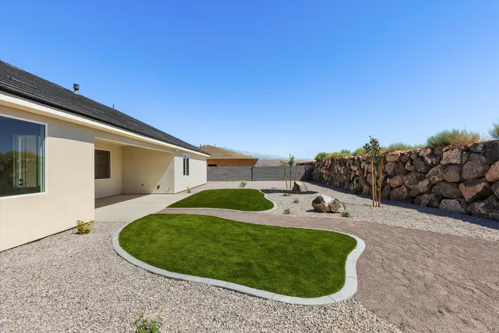 Expansive backyard featuring a rock retaining wall, gravel landscaping, integrated turf sections, a concrete patio, and a stucco exterior