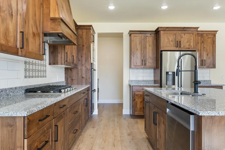 Galley-style kitchen featuring rich wood cabinetry, granite countertops, stainless steel appliances including a gas cooktop and dishwasher, white subway tile backsplash, and wood-finish flooring throughout