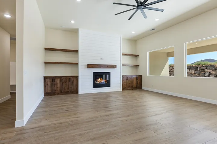 Spacious open living area featuring wood-finish flooring, a contemporary gas fireplace with white subway tile surround and wood mantel shelving, and built-in cabinetry flanking the hearth