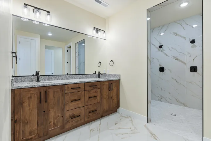 Spa-inspired primary bathroom showcasing a custom wood-finish vanity with dual sinks, granite countertop, and polished chrome fixtures