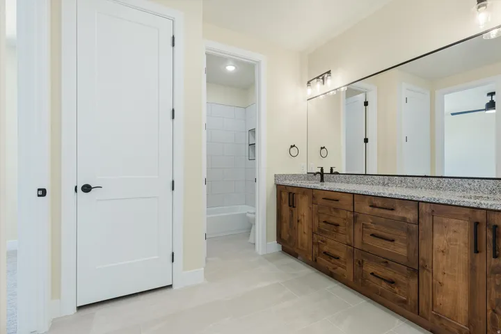 Spa-inspired primary bathroom showcasing a dual-sink vanity with warm wood cabinetry, granite countertop, and polished chrome fixtures