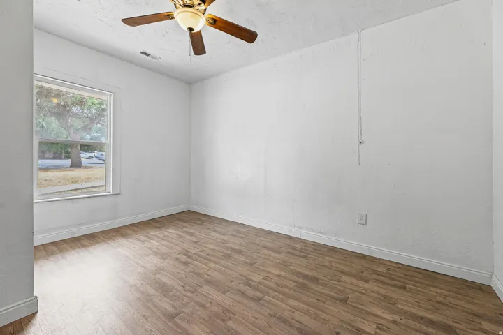 Wood-finish flooring, ceiling fan with integrated lighting, and a window with white trim