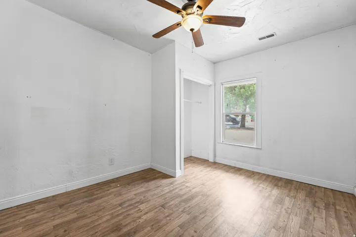 Wood-finish flooring throughout, ceiling fan with integrated lighting, and a single window with a white frame