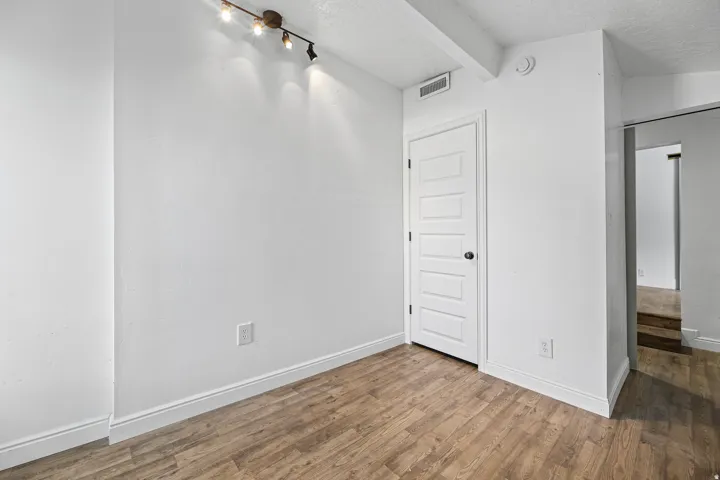 Wood-finish flooring with white baseboards and trim, white paneled door, and recessed lighting fixture