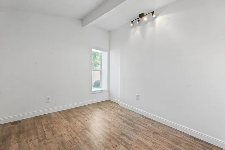 Wood-finish flooring with white baseboards, a white-framed window, and a track lighting fixture