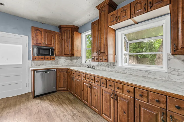 Wood-finish flooring, wood cabinetry, stone-look countertops, stainless steel dishwasher, and built-in microwave